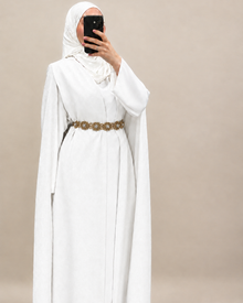 Cape mariee longue blanche Elegance Zaina Maxi portee avec une ceinture bronze en accessoire et un hijab blanc.