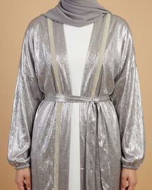 Détail du kimono pailleté argenté porté sur fond beige : galons brillants, manches et ceinture