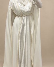 Détail de la cape blanche portée avec ceinture argentée sur fond beige