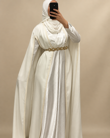Cape blanche portée sur une robe avec ceinture dorée sur fond beige