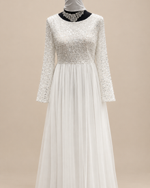 Robe de soirée blanche avec buste pailleté et manches longues sur fond beige clair
