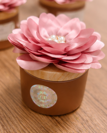 Gros plan du pot de poudre de SIDR 50 g avec couvercle doré et fleur rose, posé sur une table en bois.