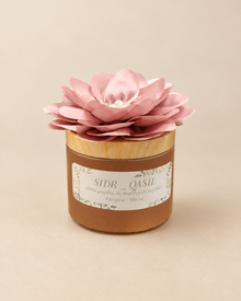 Pot de poudre de SIDR 50 g avec étiquette SIDR QASIL, couvercle doré et fleur rose, sur fond beige.