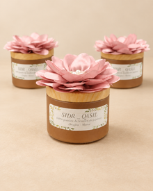 Trois pots SIDR sur fond épuré, poudre de SIDR avec couvercles dorés et fleurs roses, présentés sur un fond beige.