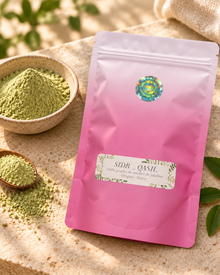  Sachet rose de poudre de SIDR à côté d’un bol et d’une cuillère en bois contenant la poudre, avec des feuilles de jujubier.